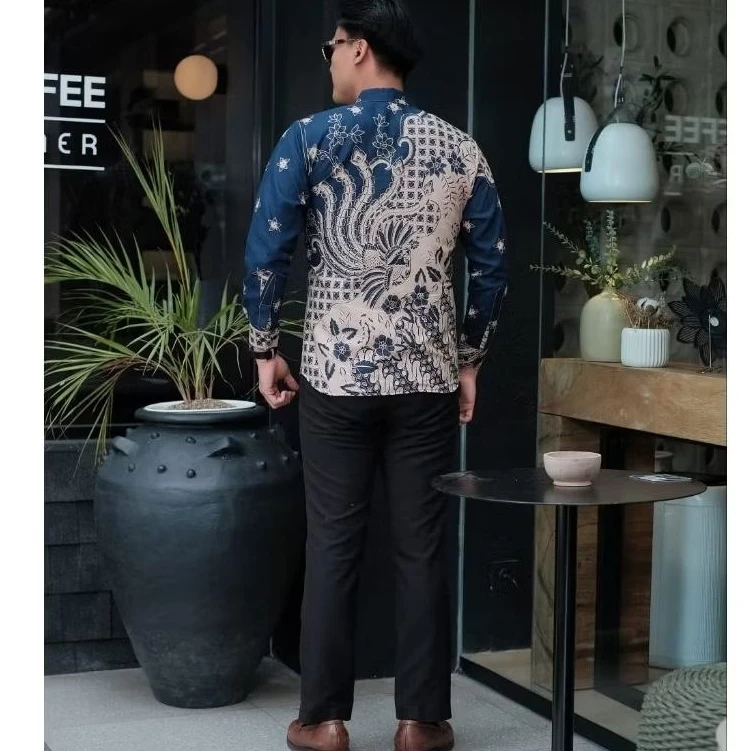 Male model in modern batik shirt featuring navy blue and beige colors with traditional Indonesian floral motifs and lattice patterns, adjusting collar outside modern cafe with sunglasses.